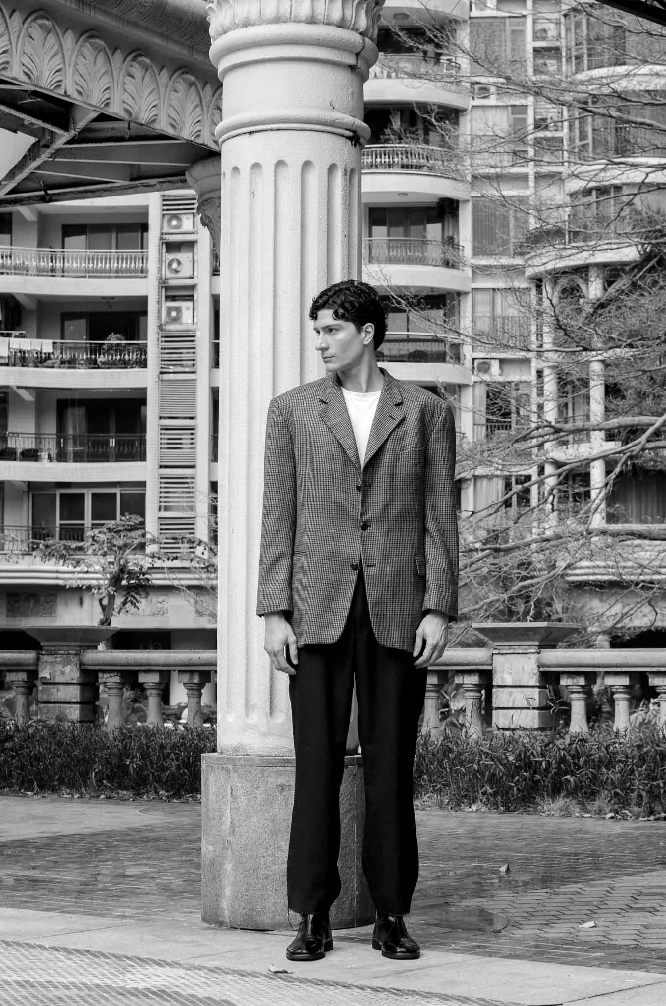 De pé junto a uma coluna clássica, de blazer xadrez